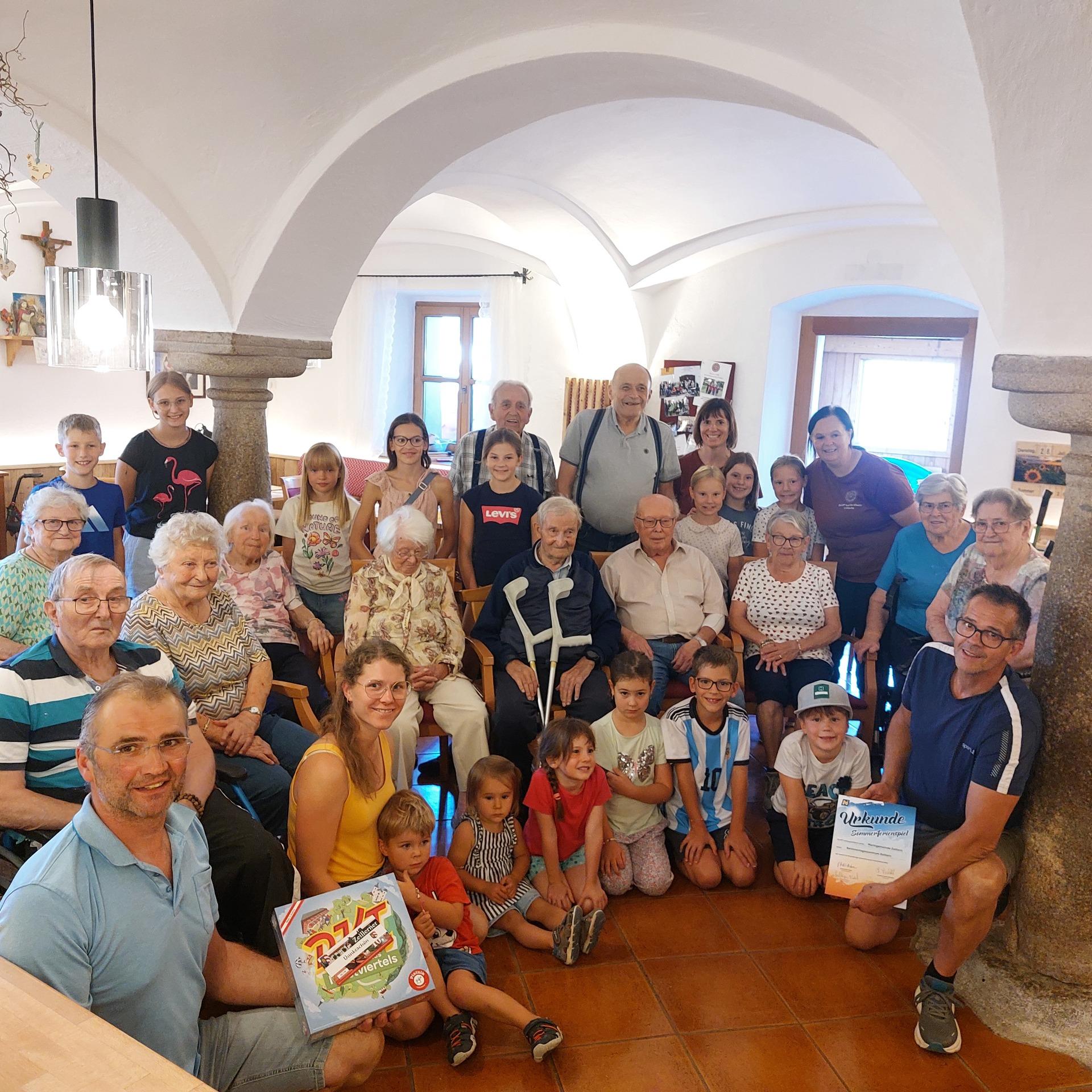 Großfamilie feiert im Innenhof mit Gewölbe, ein Mann hält ein Spiel, ein Mann hält Urkunde